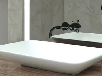 A white limestone single basin and faucet next to a lighted mirror in Qatar.